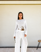Woman wearing a white crochet outfit standing in front of a closed shutter.