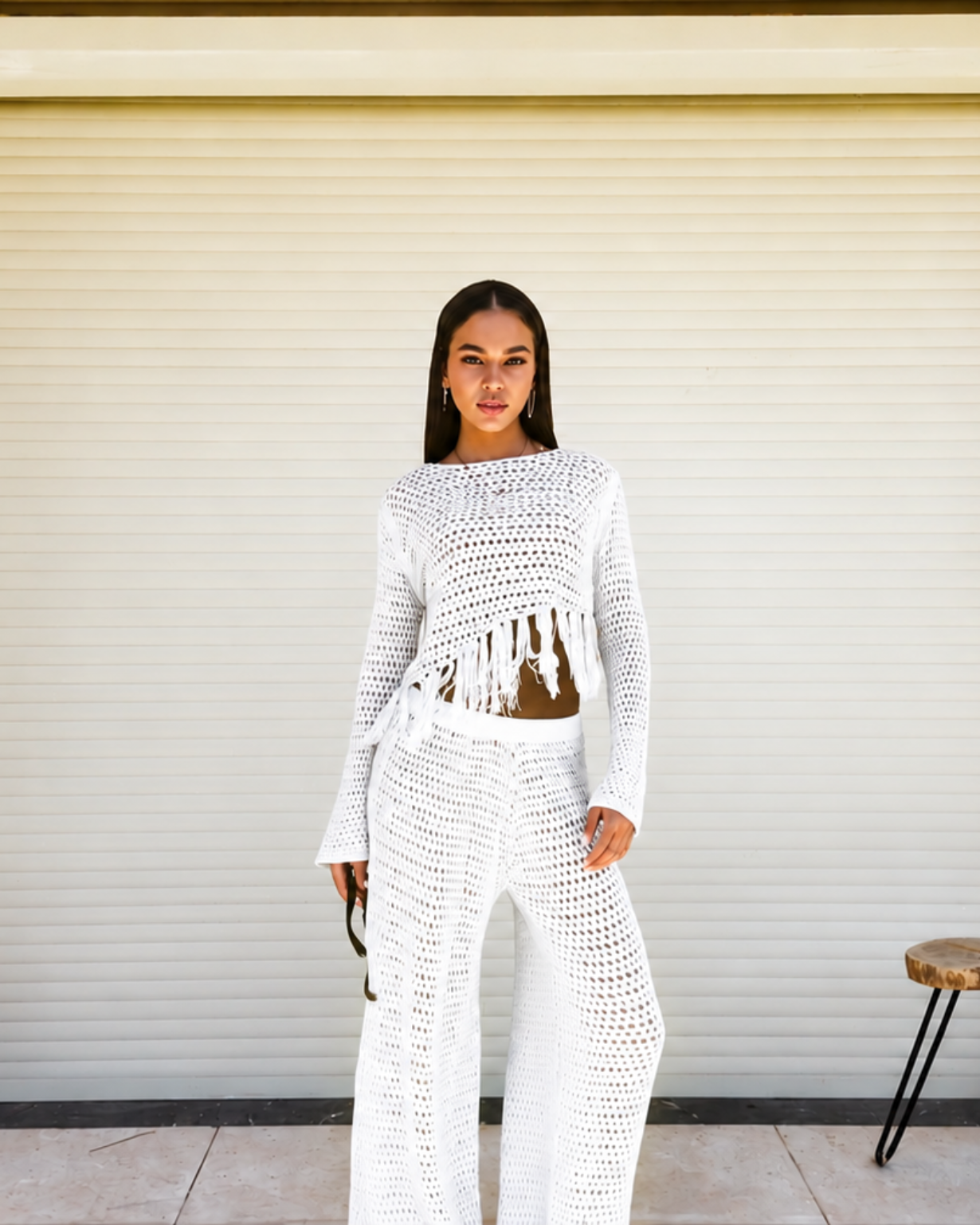 Woman wearing a white crochet outfit standing in front of a closed shutter.